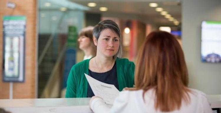 Young woman talking to another woman working on reception in a health care setting