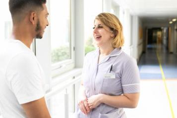 Nurse and patient chatting in hospital corridor 