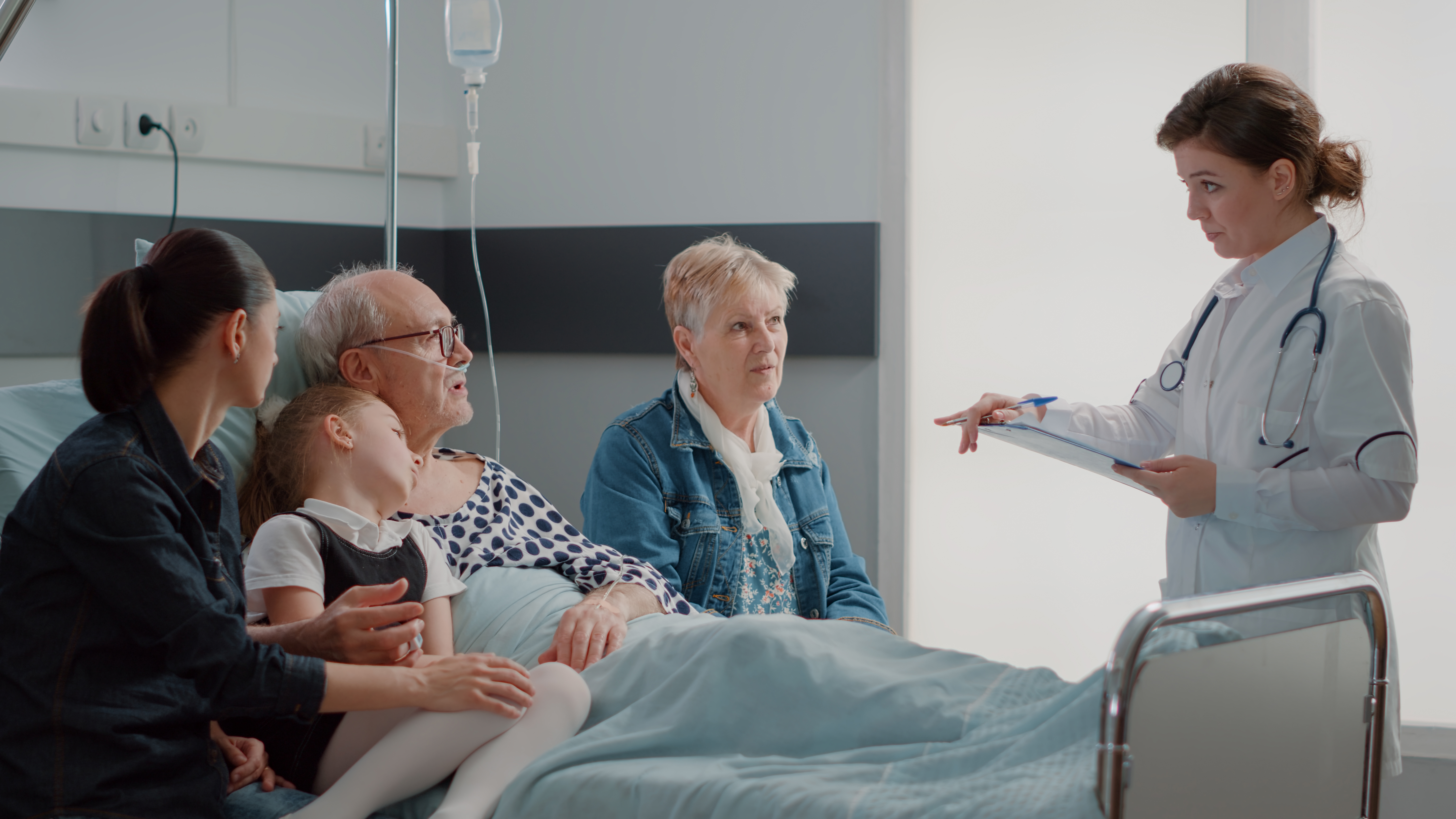 Elderly man in hospital bed, surrounded by family talking to doctor