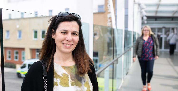Woman standing in hospital corridor smiling warmly at the camera