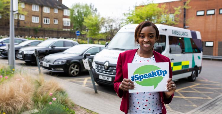 Woman holding an Healthwatch speak up sign and smiling warmly at the camera
