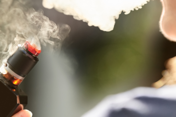 Over the shoulder view of a woman smoking an electronic cigarette or vape outdoors.