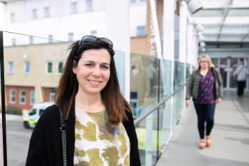 Woman standing in hospital corridor smiling warmly at the camera