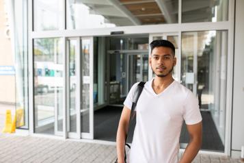 Young man looking directly at camera with slight smile on his face standing in front of a hospital