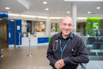 Man in medical setting wearing NHS lanyard smiling at the camera 