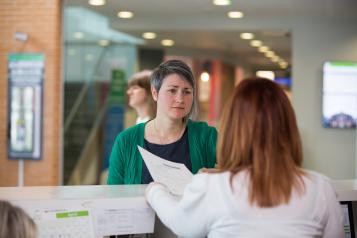 photo of woman frowning talking to a receptionist in a medical setting