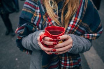 Woman holding a heart shaped mug with coffee standing outside
