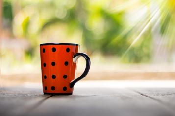 Red cup with black spots on a table with trees in the background
