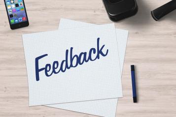 A desk with a piece of paper with feedback written on it and a mobile phone next to it.